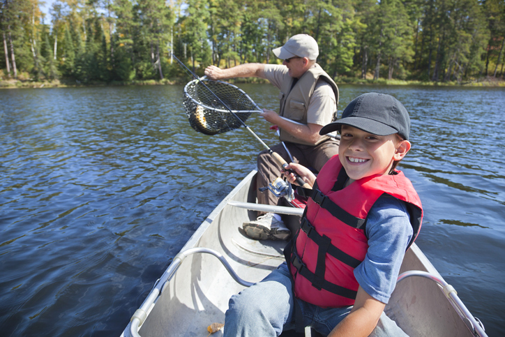 Young boy fisherman smiles while his dad takes the fish out of the net