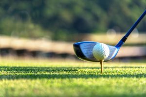 Close up golf ball and driver, player doing golf swing tee off on the green sunset evening time, presumably does exercise. Healthy and Lifestyle Concept.