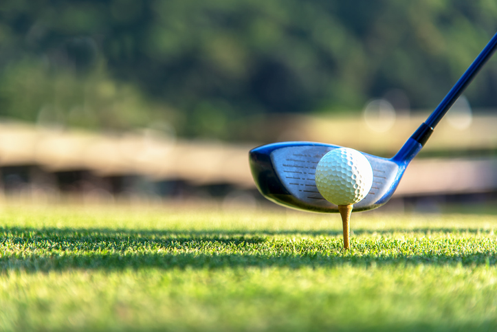 Close up golf ball and driver, player doing golf swing tee off on the green sunset evening time, presumably does exercise.  Healthy and Lifestyle Concept.